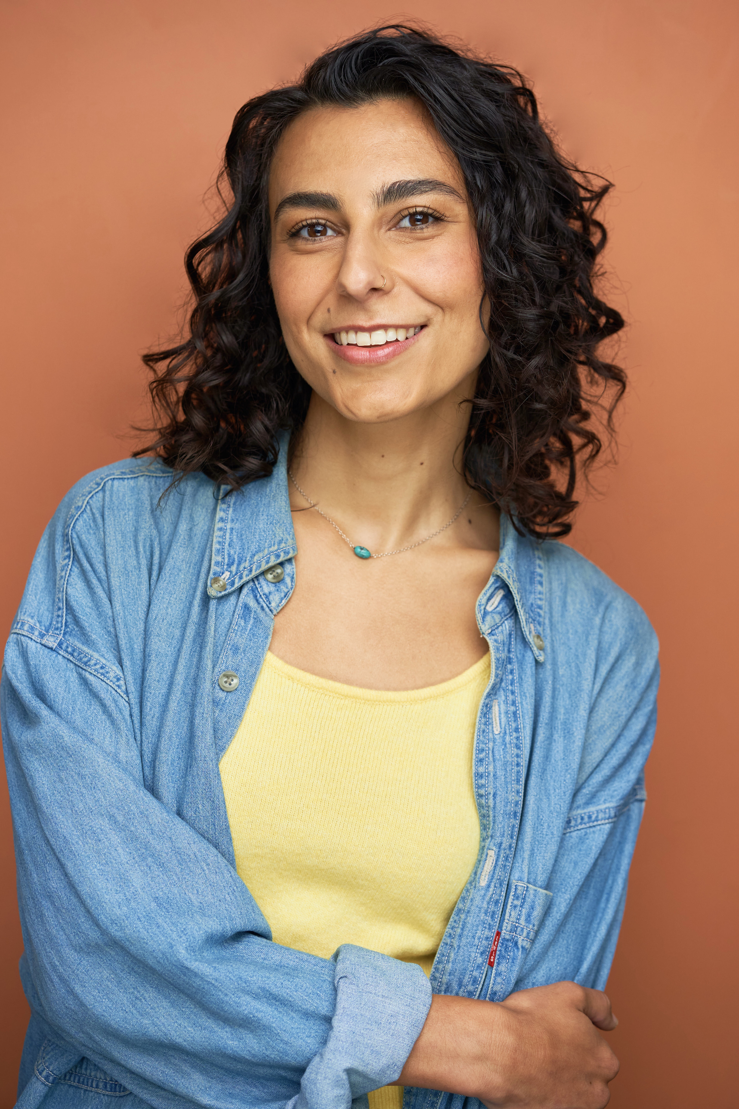 Headshot of Mari Vial-Golden in a yellow tank-top and blue denim overshirt. She is smiling and looking at the camera. Photo by Shani Hadjian.